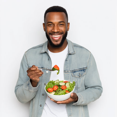 A cheerful man enjoys a fresh salad in a bright studio, promoting healthy eating.の素材