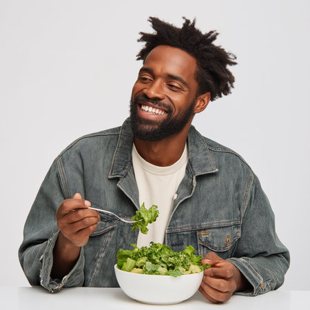 Smiling man relishes a healthy bowl of greens in a clean studio during the day.の素材
