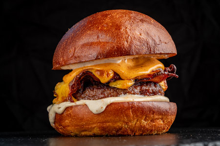Succulent bacon cheeseburger stacked high with gooey cheese and rich sauce, perfect for food lovers.の写真素材