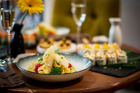 A plate of pasta with colorful veggies sits beautifully at a table with fresh flowers.の写真素材