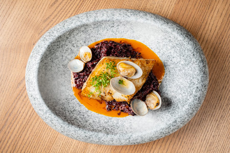 Cod fillet is beautifully plated with black rice and clams, showcasing vibrant colors and textures.
