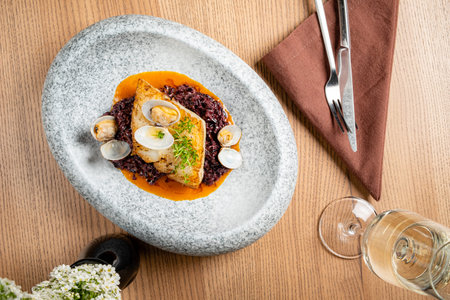 A stunning fish dish on a textured stone plate, paired with black rice and clams.