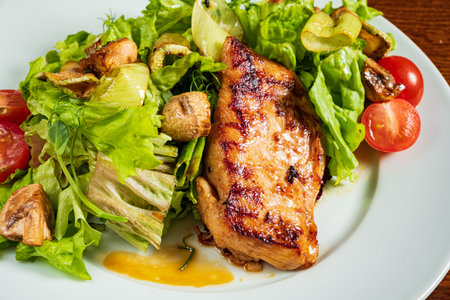 Savory grilled chicken rests atop crisp lettuce with colorful tomatoes and mushrooms surrounding it.の写真素材