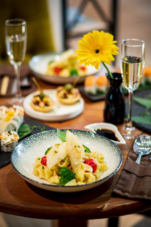 A tasty plate of pasta with fresh vegetables sits on a wooden table, surrounded by sushi and drinks.の写真素材