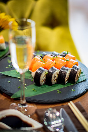 Colorful sushi rolls on a dark slate plate with a sparkling drink in a cozy setting.の写真素材