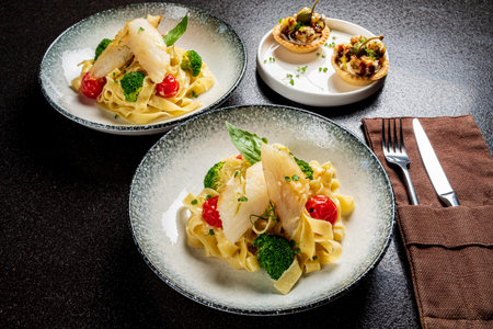 Two bowls of fettuccine with vibrant broccoli and tomatoes served alongside tasty appetizers.