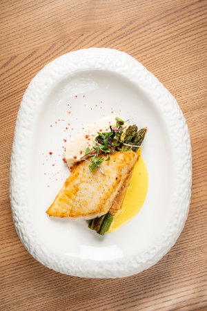 A beautifully plated dish features grilled fish alongside asparagus and a rich sauce.