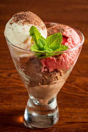 A tasty dessert of chocolate, strawberry, and vanilla ice cream in a glass bowl with mint.の写真素材