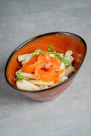 Salmon artfully placed atop creamy pasta, beautifully garnished with fresh herbs in a bowl.