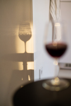 Delicate wine glass stands on a table, creating a beautiful shadow on the wall during the evening.の写真素材