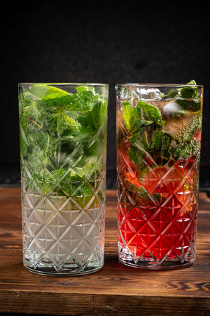 Two tall glasses filled with mint leaves and colorful drinks await enjoyment on rustic wood.の写真素材