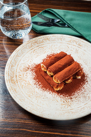 Layers of rich tiramisu dusted with cocoa powder are beautifully arranged on a decorative plate.の写真素材