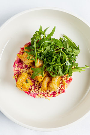 A gourmet dish featuring shrimp on a bed of colorful couscous, topped with fresh arugula.