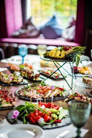 Delicious array of salads, fruits, and snacks shared during a joyful gathering in a cozy setting.の写真素材