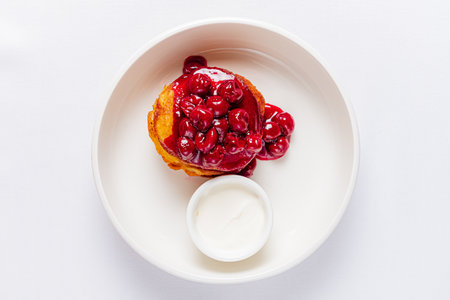A fluffy pancake sits invitingly on a plate, topped with vibrant cherries and a side of cream.の写真素材