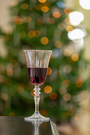 A crystal glass holds red liquid, set against a glowing Christmas tree in a festive atmosphere.の写真素材