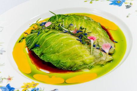 Fresh cabbage leaves are creatively arranged with vibrant sauces and edible flowers.の写真素材