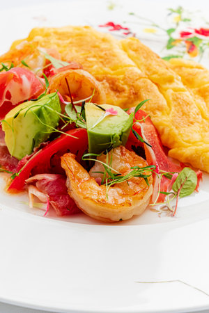 A vibrant shrimp omelet is served alongside a colorful salad of fresh vegetables and herbs.の写真素材