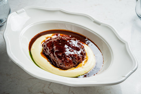 Richly glazed meat sits atop velvety puree, inviting indulgence in a charming dining setting.の写真素材