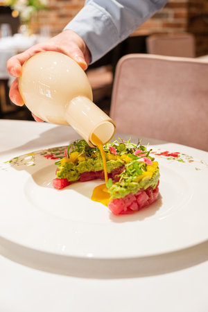 A chef drizzles vibrant sauce on tuna tartare, highlighting skill in a stylish setting.の写真素材