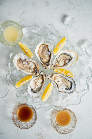 Enjoy a platter of fresh oysters on ice, elegantly garnished with lemon and paired with drinks.の写真素材