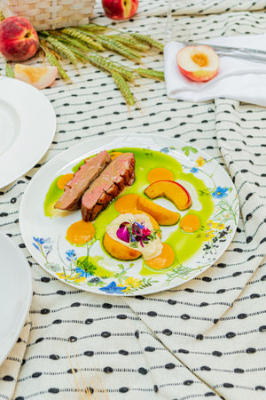 A picnic feast presents exquisite duck breast artfully arranged with fresh peach slices and flowers.の写真素材