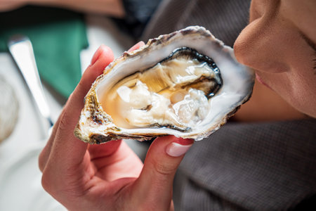 A person holds a fresh oyster, ready to savor its briny flavor at a seaside eatery.の写真素材