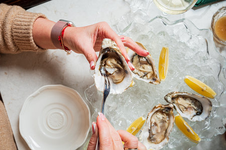 A pair of hands savor the moment, delicately handling oysters on ice with lemon.の写真素材