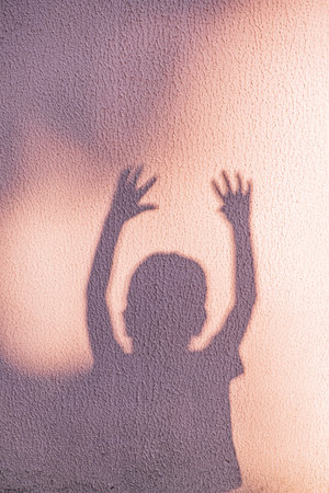 A child's shadow dances on a textured wall as they reach for the sky, celebrating daylight.の写真素材