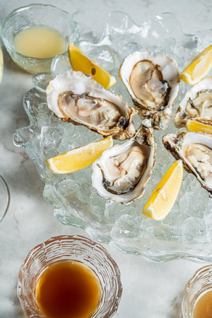 Succulent oysters arranged on a cool platter with ice, paired with zesty lemon and sauce.の写真素材