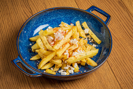 Crispy fries covered with crumbled cheese and sprinkled with spices, served in a blue bowl.