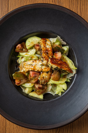 Crisp lettuce and vibrant tomatoes combine with juicy grilled chicken in a deep bowl.の写真素材