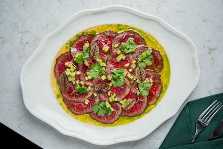 Beef carpaccio artfully arranged on a white dish, topped with herbs and sauces, ready to enjoy.