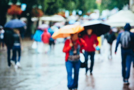 Crowds walk through a bustling street under rainy skies, carrying bright umbrellas amidst puddles.の写真素材