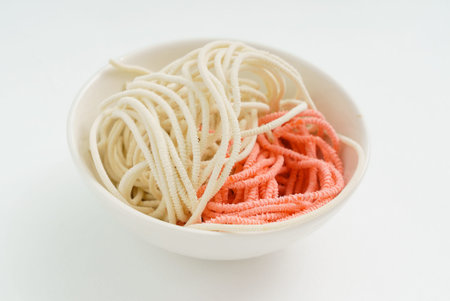 A bowl holds strands of noodles, featuring playful colors of pink and white, inviting tasty meals.