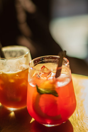 Two colorful cocktails sit on a wooden table, showcasing vibrant ingredients and ice.