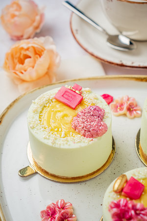 Tempting pastel mini cakes sit gracefully on a tray, surrounded by lovely blossoms and coffee.