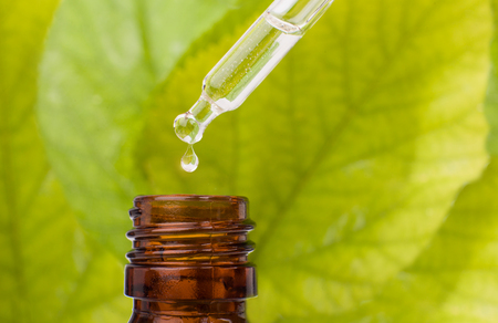 Dropper over essential oil bottle. Dropper with brown bottle and green background.の写真素材