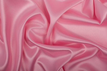 Pink satin fabric as background. Abstract luxury cloth or liquid wave.の写真素材