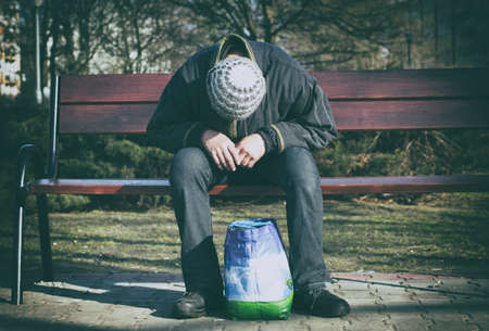 Depressed and hopeless - a man sitting alone after drugs and alcohol on a wooden bench.の写真素材