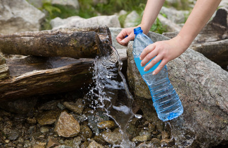 Taking spring water from a mountain spring. Plastic bottle water filling, natural pure water source.