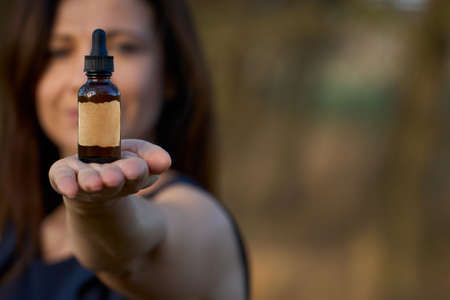 Woman holding a bottle of dietary supplements or essential oil in her hands. The concept of alternative medicine. Cop space and empty label.の写真素材