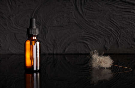 Amber glass dropper bottle with black with dry plants on dark background. Skin care products, natural cosmetics. Beauty concept for face and body care. Mock up for product.の写真素材