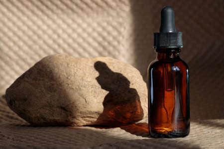 Skin care essential oil glass bottle with dropper and stone paper background. Moisturizing serum for facial skin. Aesthetics, minimalism.の写真素材