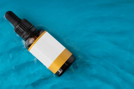 Amber cosmetic bottle on water surface. Summer water pool fresh concept. Flat lay, top view. MOCKUP, copy space.の写真素材