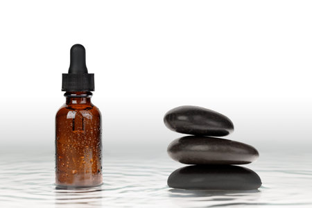 A mock-up of a minimalist, zen-style bottle with a dropper. Black stones and water, skin hydration....