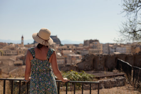 A tourist girl looks at the historic skyline of Corfu town in Greece. Back view of traveler girl, vacation concept.の写真素材