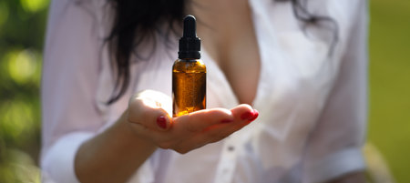 Cosmetic bottle on hands, blurred silhouette of sexy woman. Amber cosmetic hand dropper bottle.の写真素材