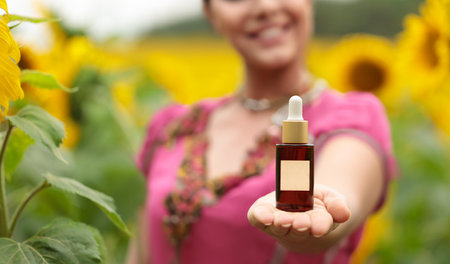 Woman holds a bottle of essential oil on her hand, blurred silhouette. Cosmetic product presentation, mockup.の写真素材