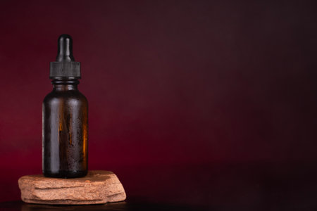 Amber Dropper Bottle on Natural Stone Pedestal with Elegant Maroon Backdropの写真素材